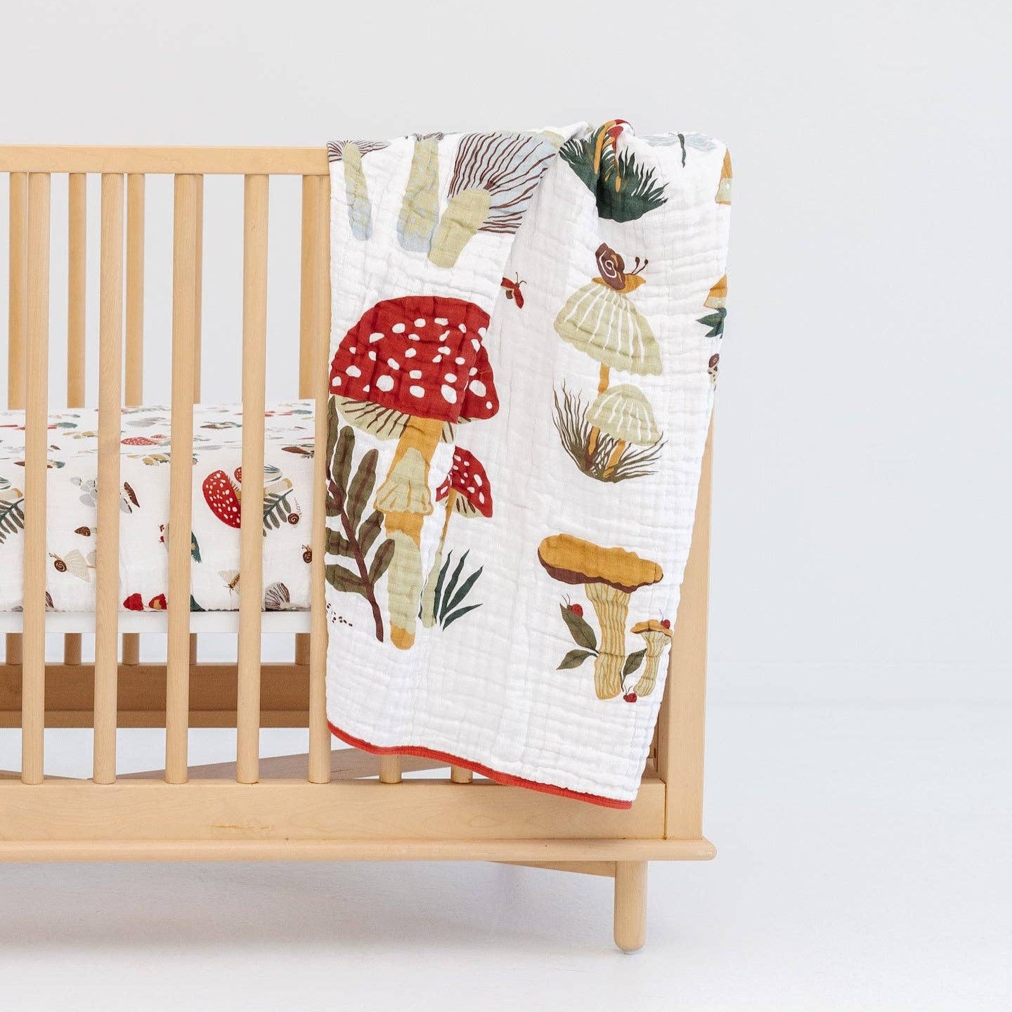 Wooden crib with a colorful mushroom-patterned quilt draped over it on a white background