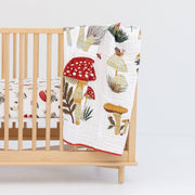 Wooden crib with a colorful mushroom-patterned quilt draped over it on a white background